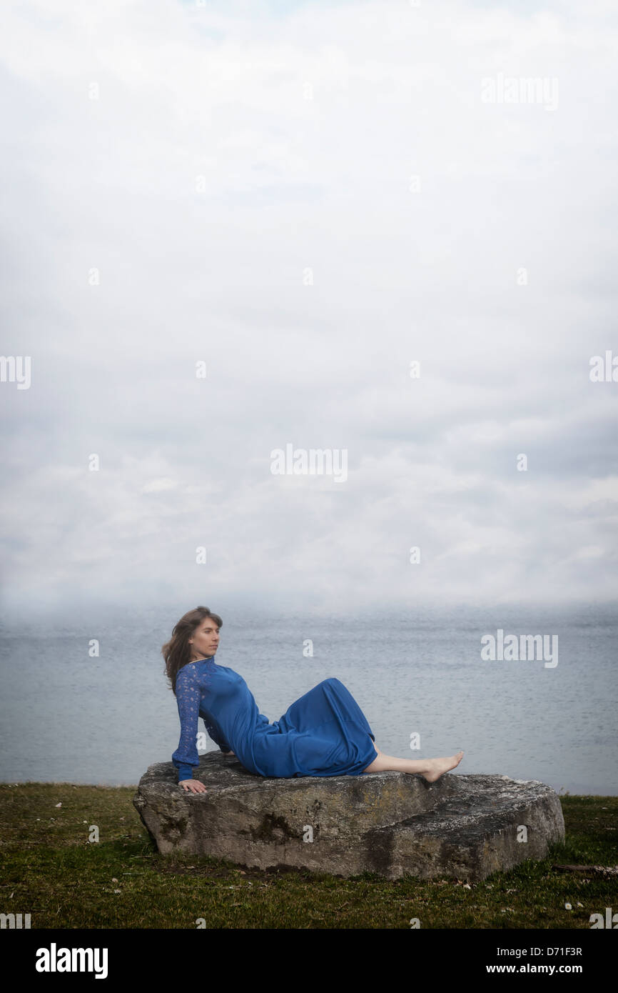 eine Mädchen in einem blauen Kleid ist auf einem Stein liegen. Stockfoto