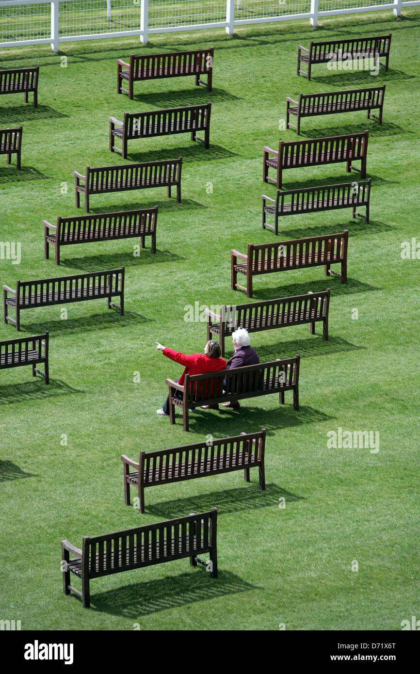 Ein paar Rennen Gänger saß auf einem der ersten Rennen der Saison Frühling in Newbury Racecourse in einem Meer von Gartenbänke Stockfoto