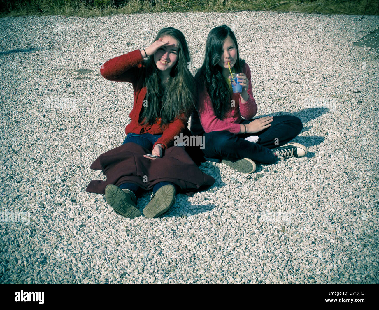 Zwei Schwestern auf Schotter in der Sonne sitzen Stockfoto