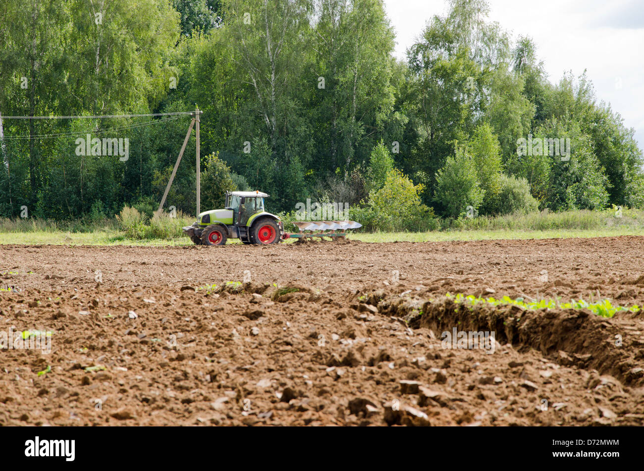 schwere Maschine Traktor Pflug Landwirtschaft Feld Ende des Sommers in der Nähe von Wald. Stockfoto