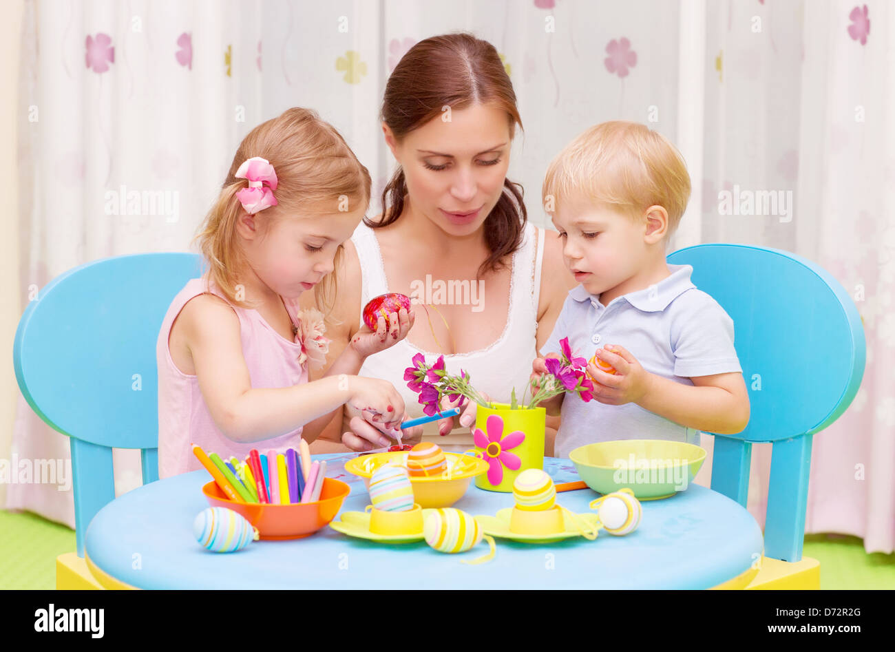 Schöne junge Mutter mit zwei süßen Kindern dekoriert traditionelle Ostereier mit bunten Farben, glücklich Familienkonzept Stockfoto