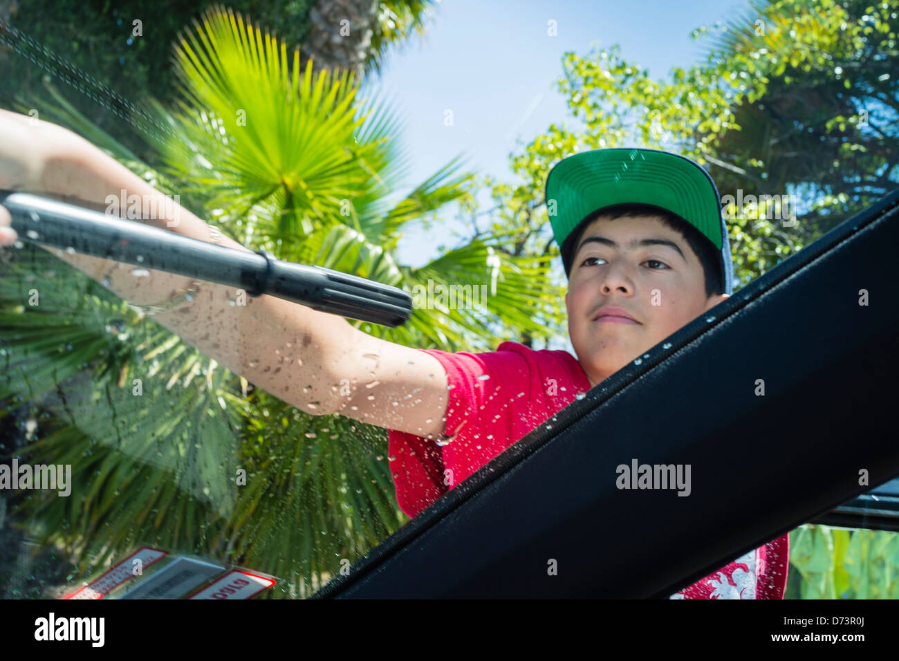 Männliche Teenager in eine Baseball-Cap verwendet eine Rakel ein Fenster eines Autos in einer High-School-Fundraising-Autowaschanlage zu trocknen. Stockfoto