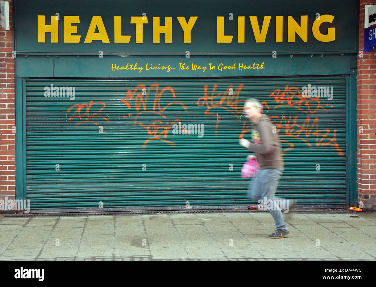 Mann hinter geschlossenen Healthy Living Shop, Joggen, Bell Street, Wigston, Leicester, England, UK Stockfoto