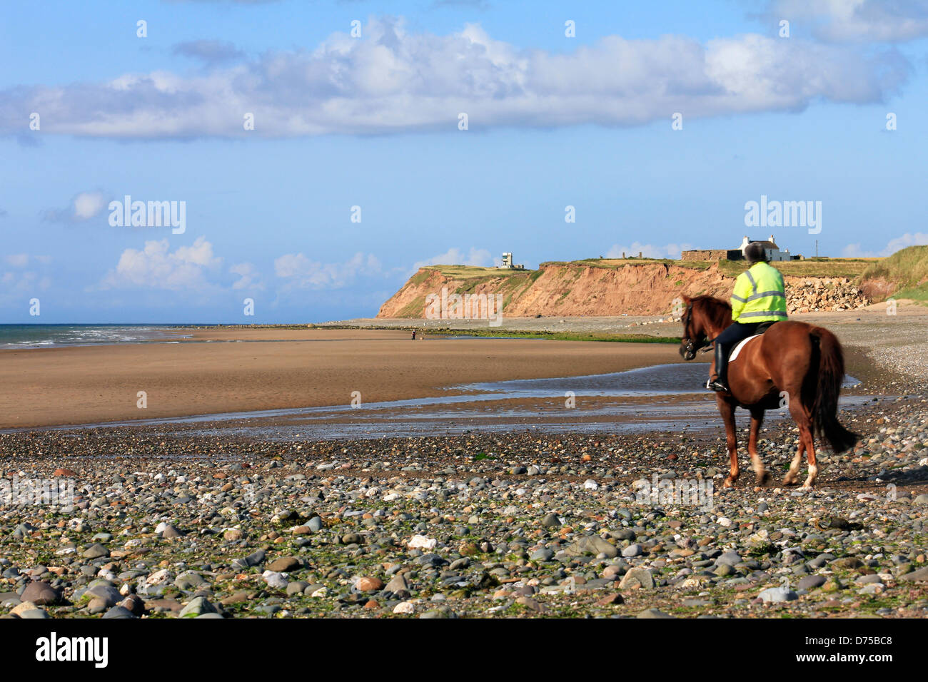 Reiterin Reiten auf einem Kiesstrand bei Ebbe vor blauem Himmel mit weißen Wolken Stockfoto