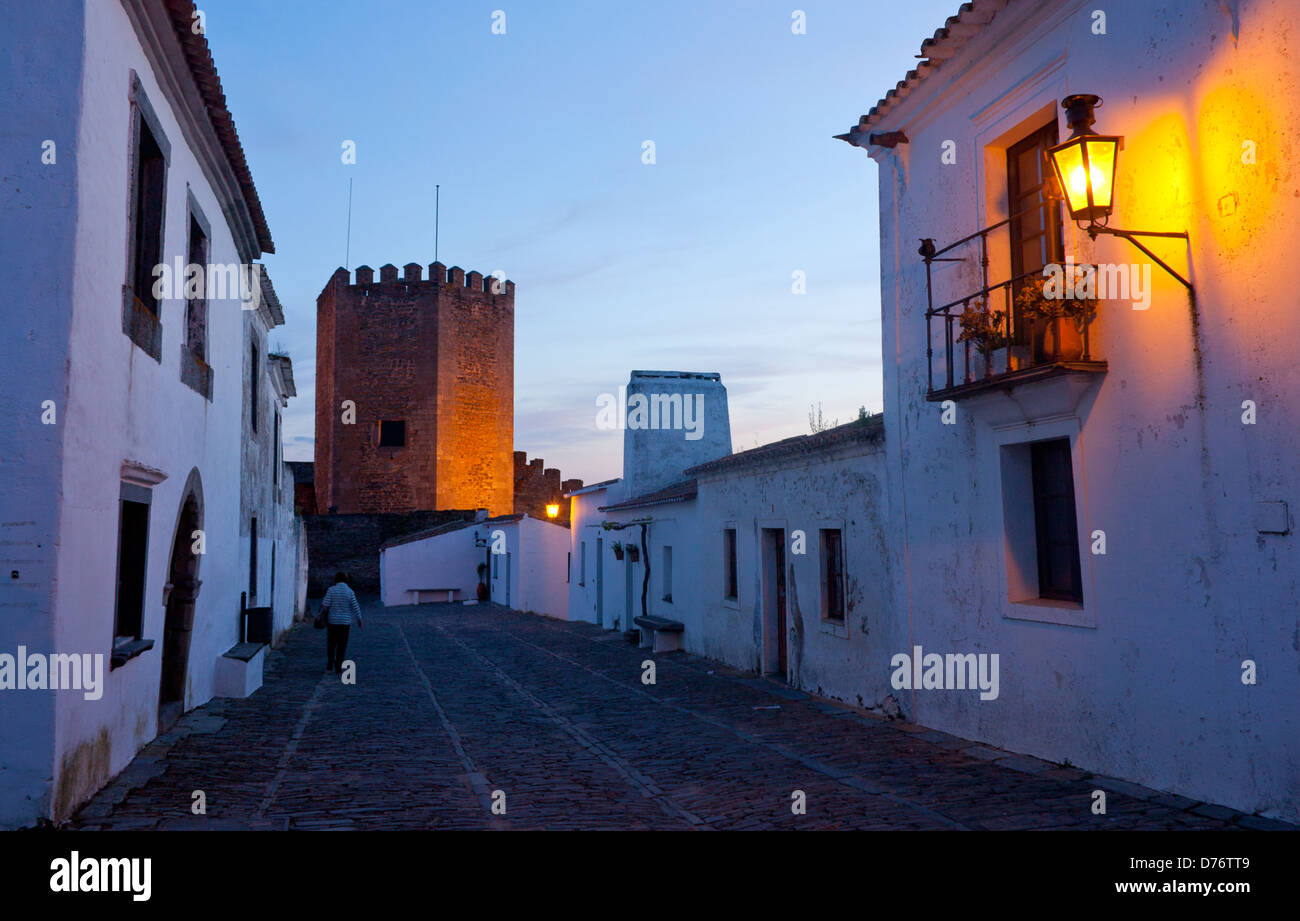 Burg und gepflasterte Straße mit Frau zu Fuß in der Dämmerung / Dämmerung / Sonnenuntergang / Abend Monsaraz Dorf Alentejo Portugal Stockfoto