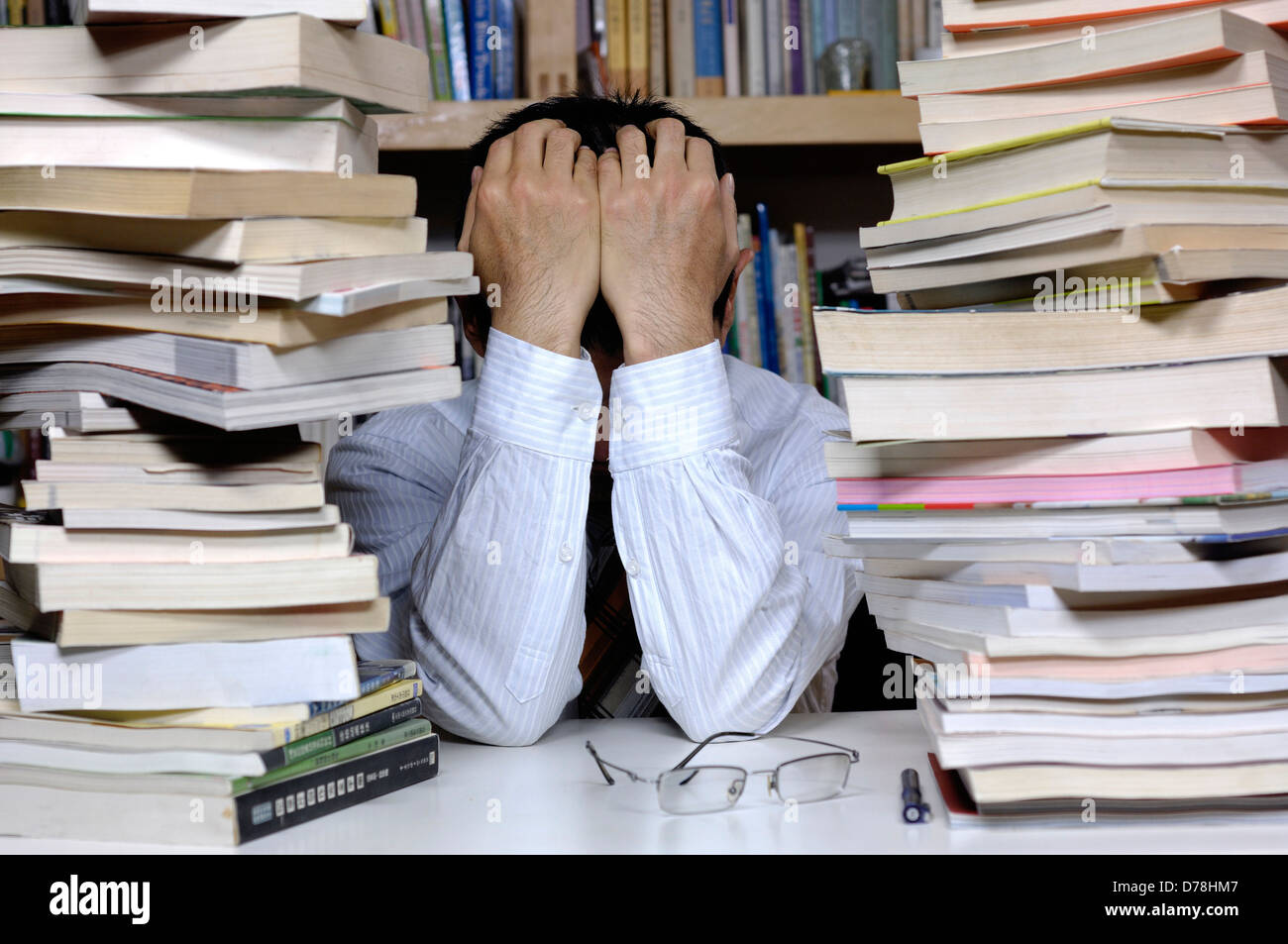 ein Mann mit beiden Händen über den Kopf, sitzt unter Haufen Bücher. Stockfoto