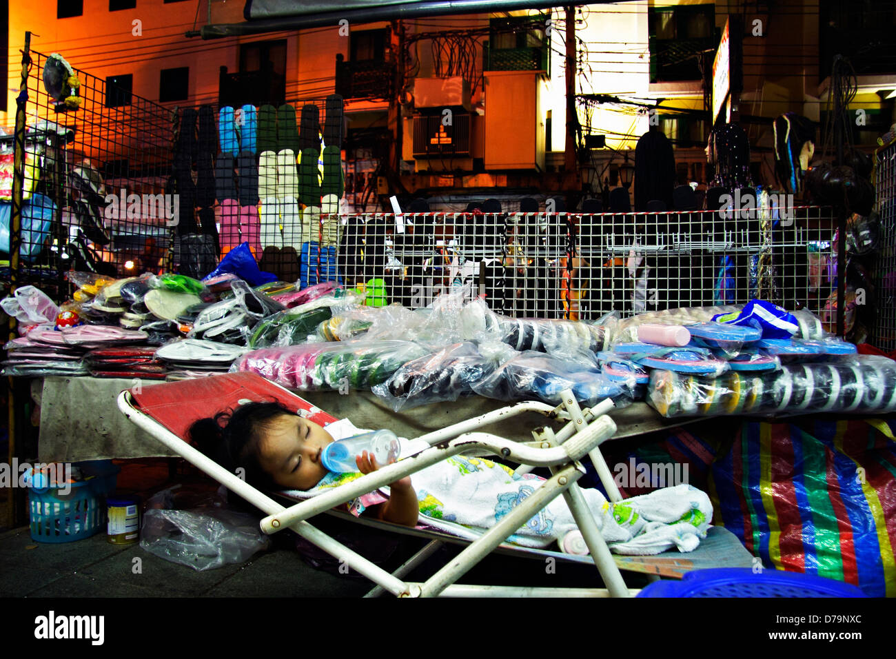 Schlafend Thai baby Mädchen trinken von ihrer Babyflasche in der verkehrsreichen und Khaosan Road, Bangkok, Thailand Stockfoto