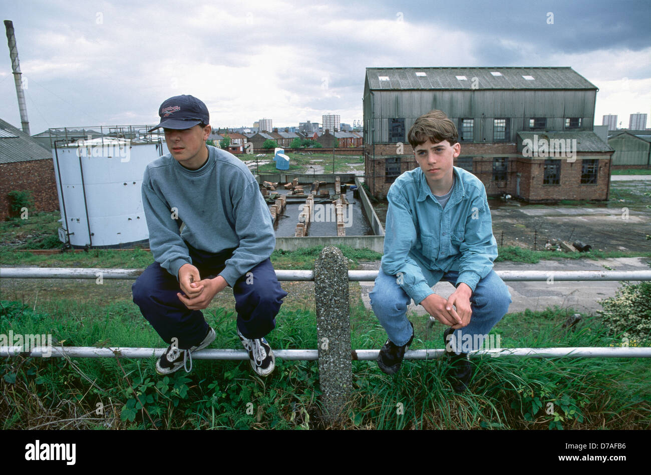 Zwei Jungs, die verlassen aussahen, sitzen auf Geländern vor der stillgelegten Teerfabrik Mitte der 1990er Jahre, Bootle, Merseyside Stockfoto