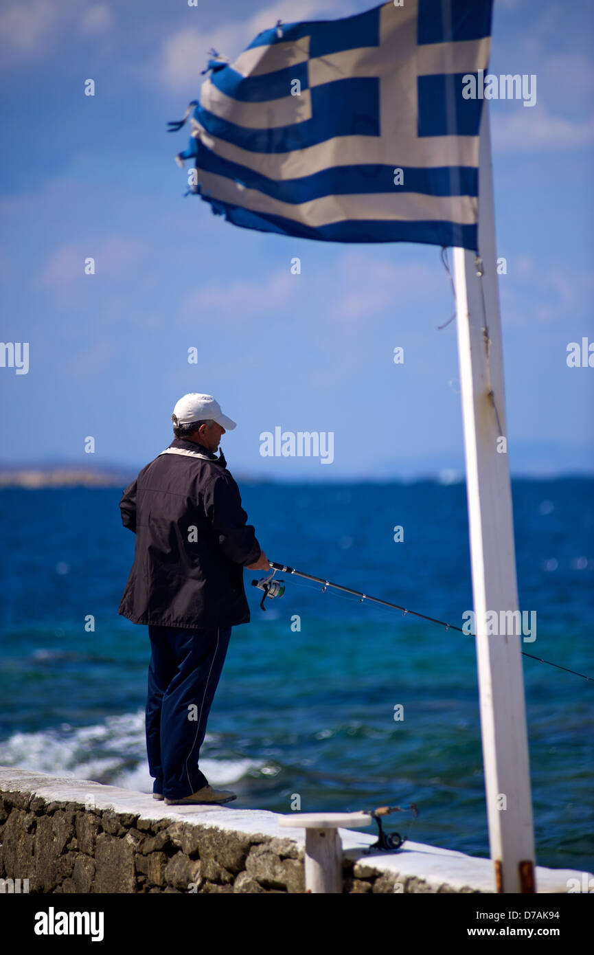 Ein Mann unter einer verwahrloster griechische Flagge in Mykonos Griechenland Angeln. Stockfoto