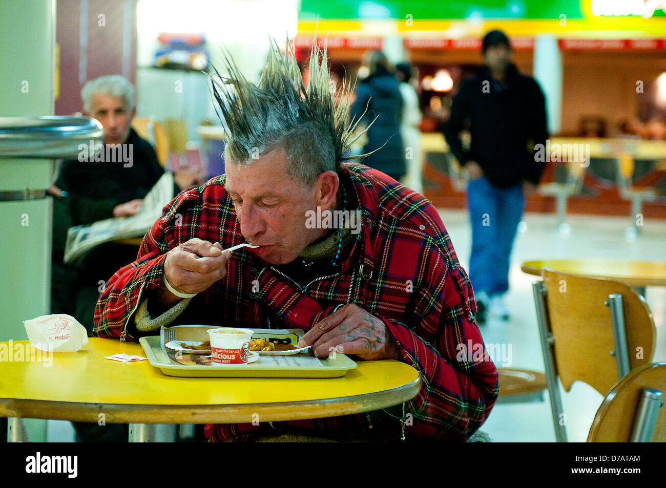 Ein älterer Mann mit einer Mohawk Haare Stil und Tartan Jacke isst von einem Fast-Food-Restaurant in London. Stockfoto
