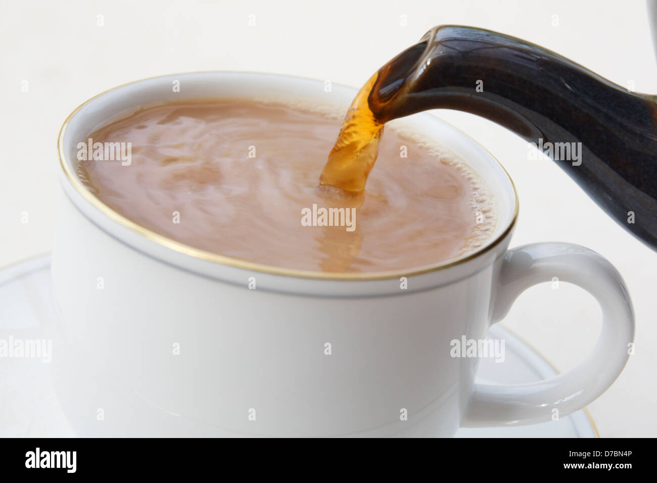 Machen Gießen einer traditionellen britischen englischen Tasse Tee aus einer Teekanne Auslauf in eine weiße porzellan Teetasse mit Milch in erster gesetzt. England Großbritannien Großbritannien Stockfoto