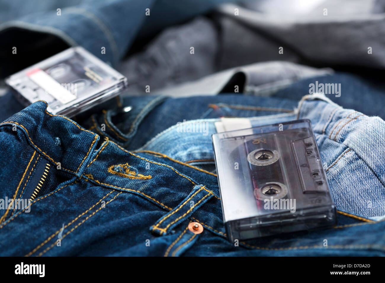Ein paar leere Audio-Kassetten, einer von ihnen noch in den Kasten gelegt auf dem Hintergrund der verschiedenen paar Jeanshosen. Stockfoto