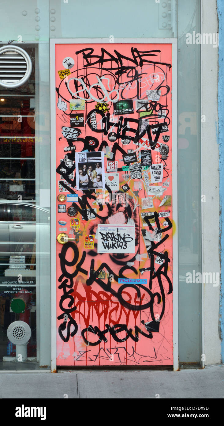 Graffiti, Aufkleber und Tags an der Tür zum Bekleidungsgeschäft Grippo Art + Design in der Grand Street in Williamsburg, Brooklyn, New York Stockfoto