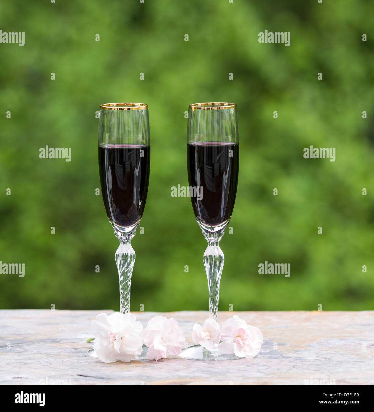 Foto von Rotwein in Gläsern mit späten Frühjahr rosa Blume auf hellen grünen Hintergrund Stockfoto