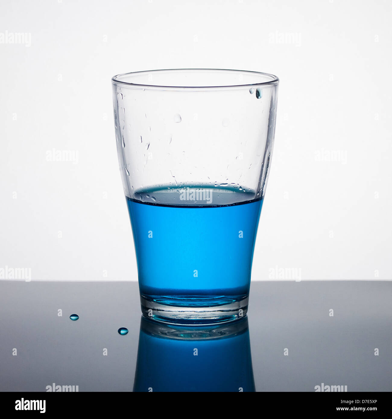 Glas halb voll von blauen Flüssigkeit auf hellem Hintergrund. Stockfoto