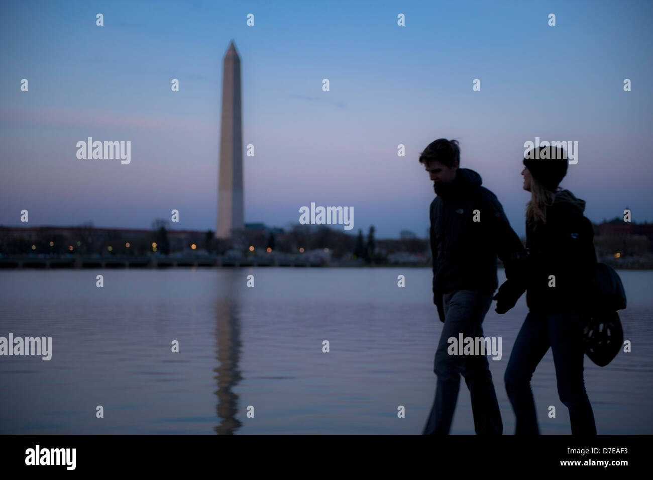 Ein junges Paar hält die Silhouette der Hände, die in der Abenddämmerung um das Washington DC-Gezeitenbecken mit dem Washington Monument im Hintergrund läuft Stockfoto