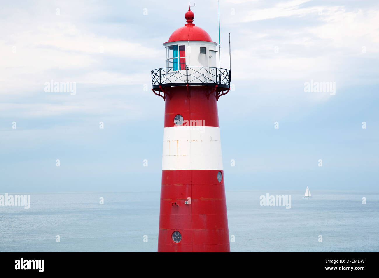 Rot-weiße Leuchtturm entlang der Küste mit einem Segelboot in der Ferne in der Nähe von Westkapelle; Zealand Niederlande Stockfoto