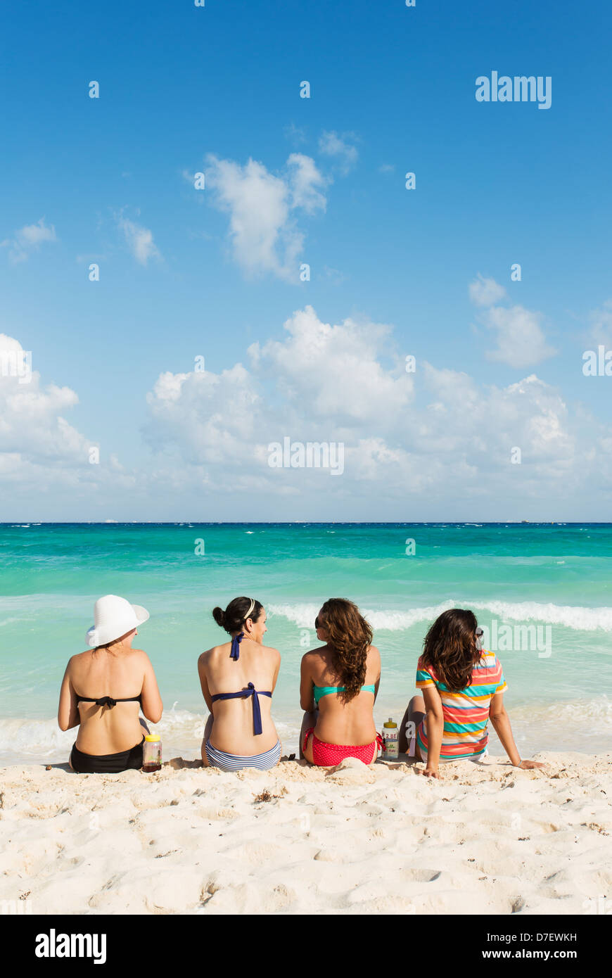 vier junge Frauen im Gespräch am Strand zu sitzen und mit Blick aufs Meer Stockfoto