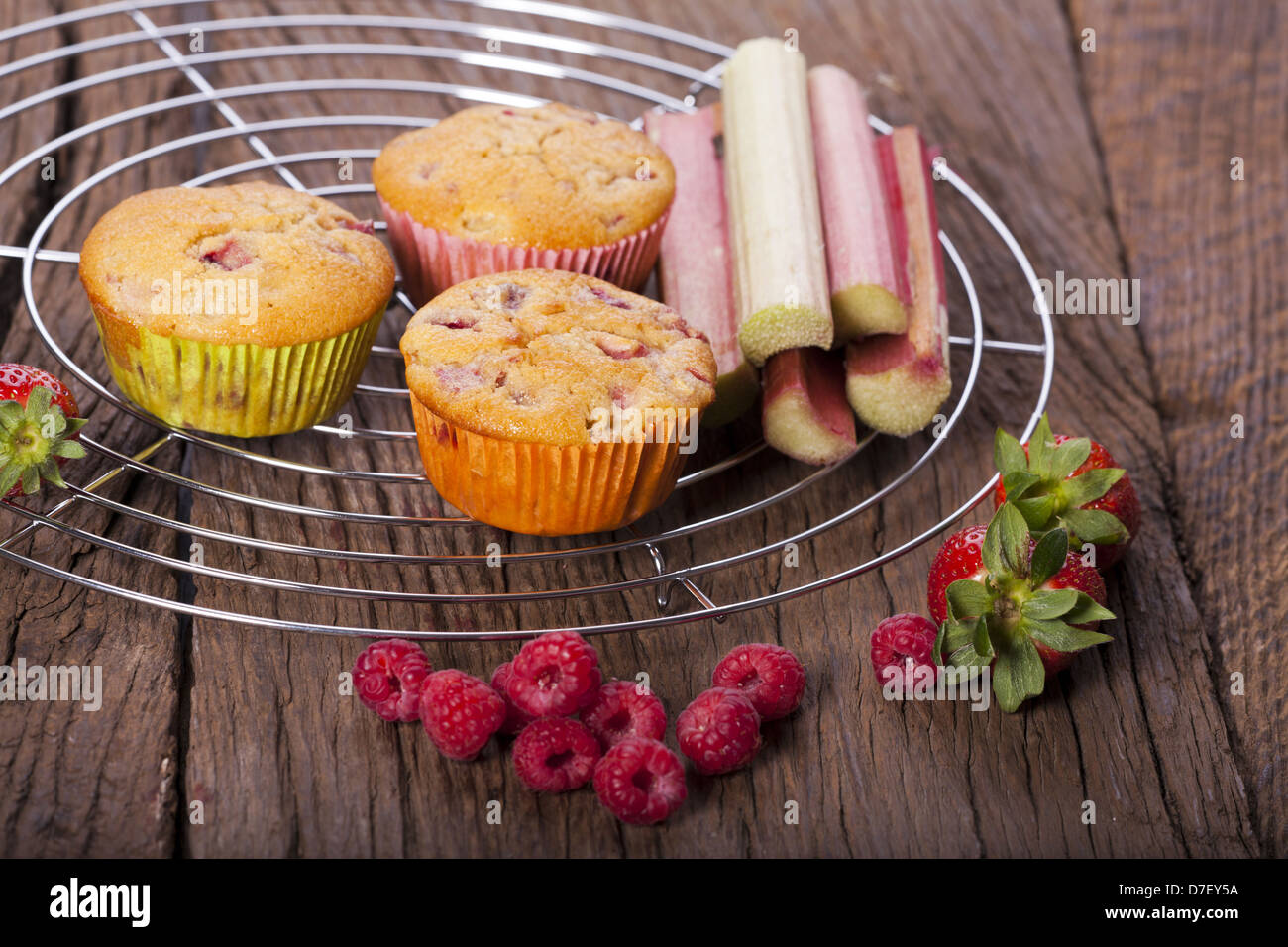 Einige ganze Erdbeere Rhabarber und Himbeer Muffins mit frischem Obst auf einem Kuchengitter Kuchen Stockfoto