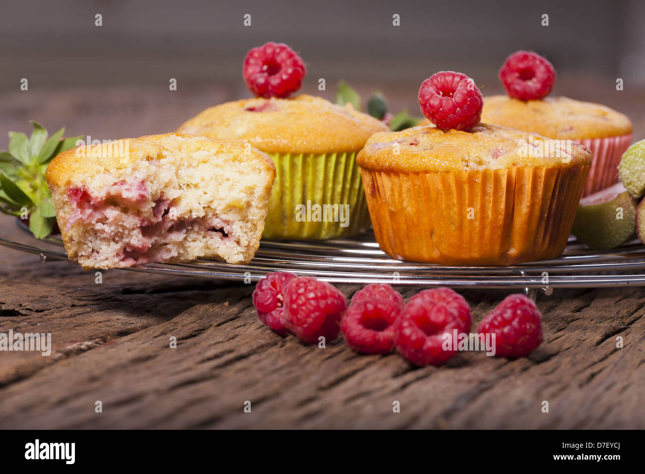 Einige ganze Muffins und eine angebissene Muffin auf einem Kuchengitter Kuchen mit frischen Himbeeren auf der Vorderseite Stockfoto