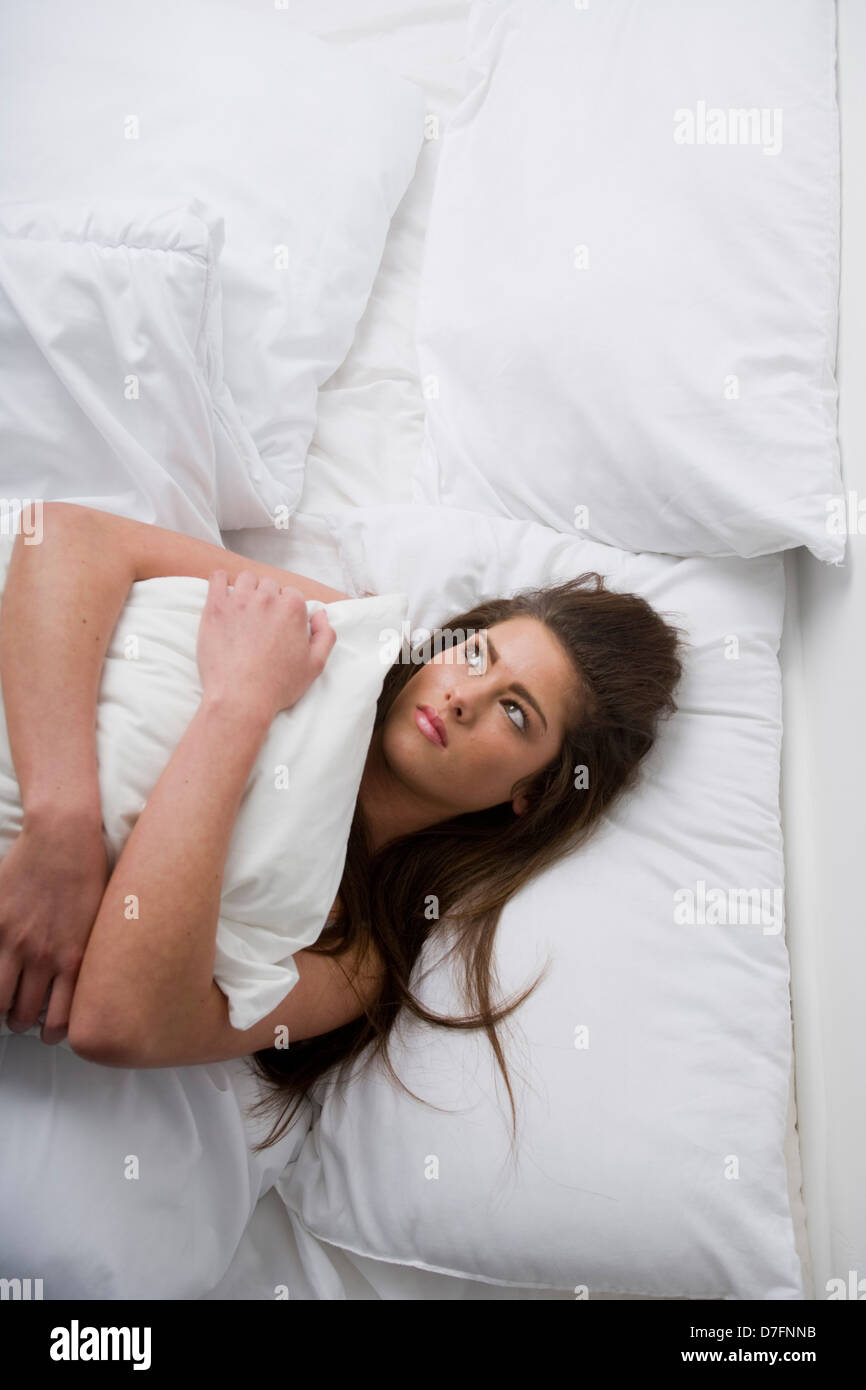 Eine traurig aussehende junge Frau im Bett umarmt eine Kissen liegend. Stockfoto