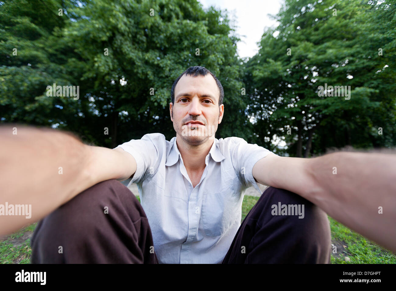 Mitte Erwachsener (Anfang 30) kaukasischen Mann schaut in die Kamera mit einem rätselhaften zuversichtlich Blick Fotografieren selbst im Park. Stockfoto