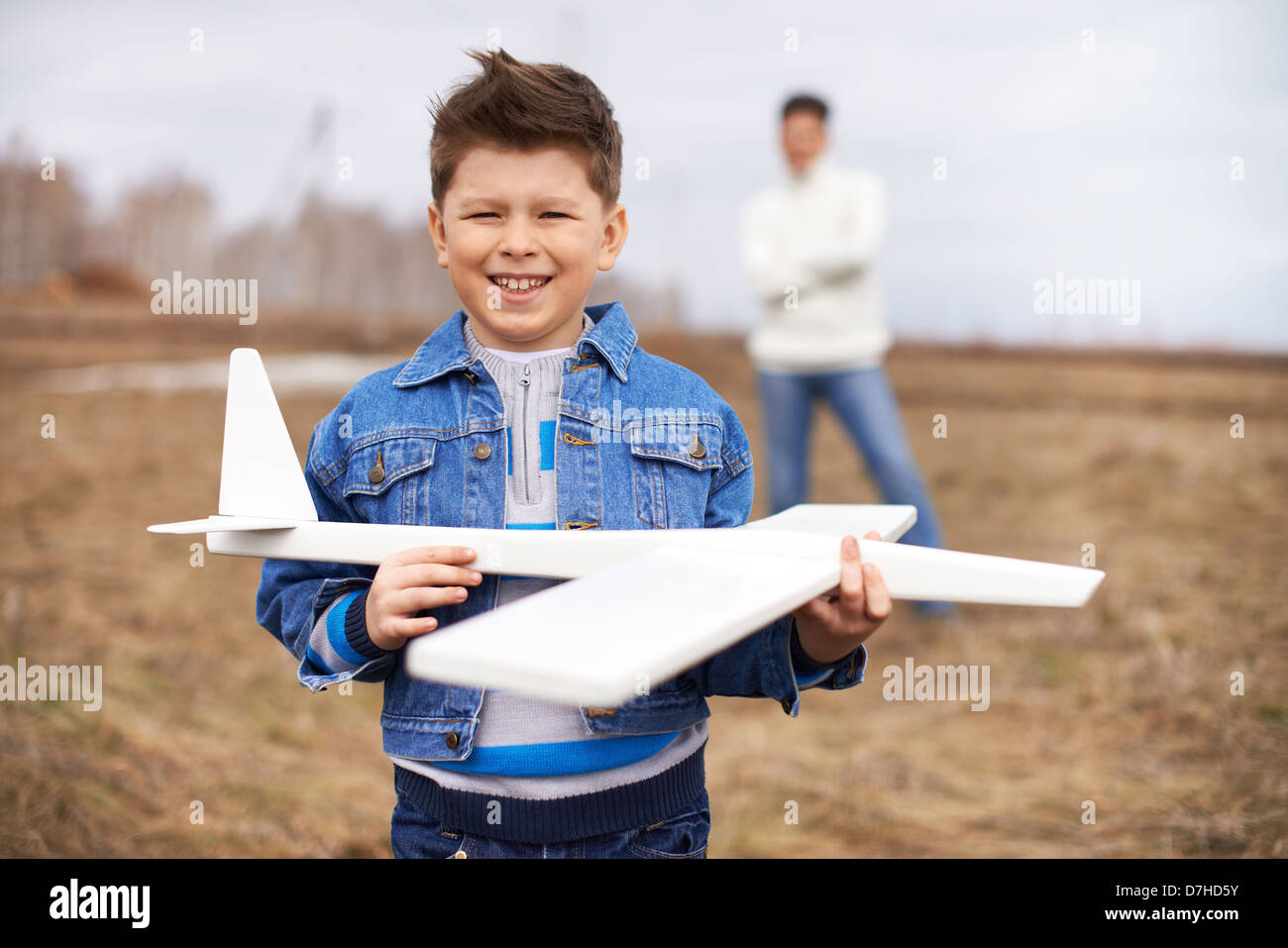 Foto von glückliches Kind mit Blick in die Kamera mit seinem Vater auf Hintergrund Spielzeugflugzeug Stockfoto