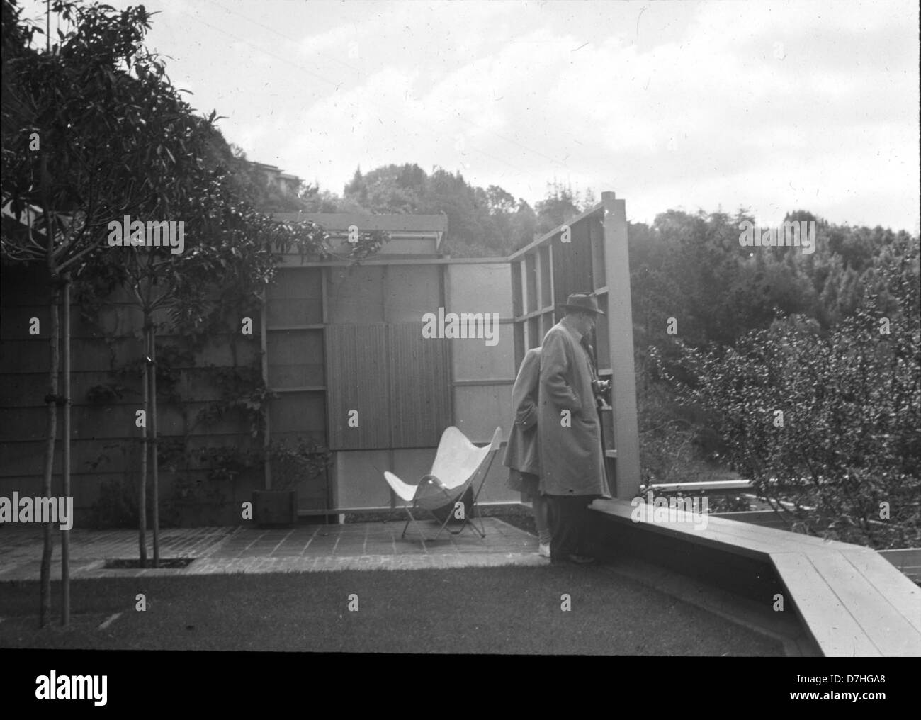 Ein Mann und eine Frau sitzen in einem Terrassenbereich mit Blick auf einen gepflegten, umzäunten Garten und halten einen ruhigen Moment der Entspannung in einer Außenumgebung fest. Stockfoto