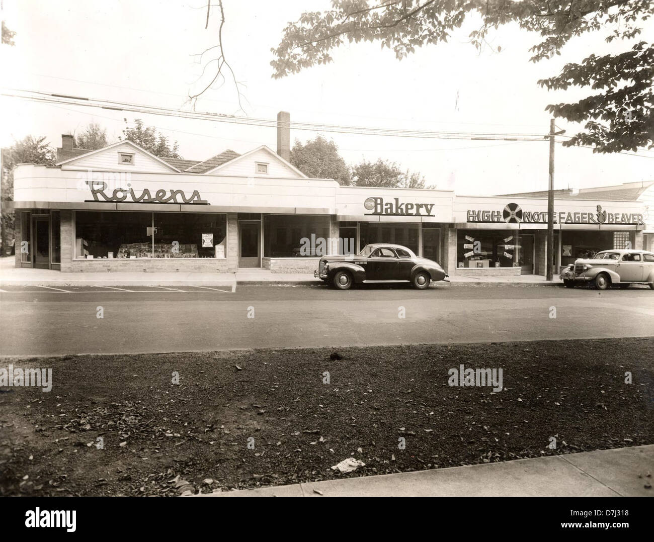 Dieses Schwarzweiß-Foto aus dem Jahr 1946 zeigt eine geschäftige Szene in der Monroe Street im Benton County mit lokalen Unternehmen wie Eager Beaver Bakery und High Note. Das Foto zeigt auch Oldtimer und Stromleitungen, die typisch für Amerika nach dem Zweiten Weltkrieg sind. Stockfoto