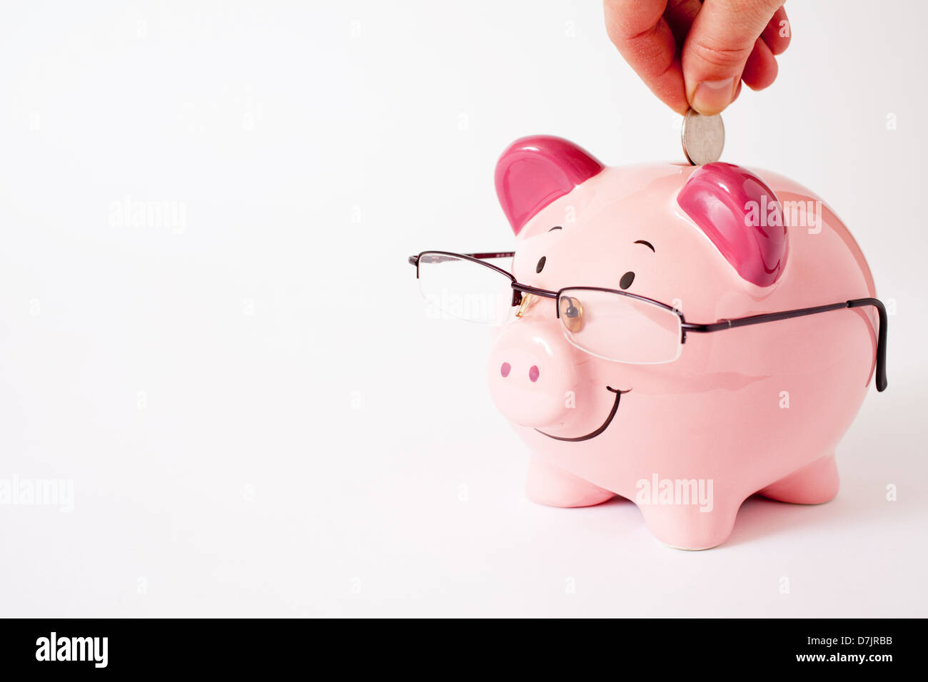 Rosa Sparschwein mit Brille, auf eine einfache Studio-Hintergrund mit einer Hand, eine Münze in den Schlitz zu Lächeln ist zurück. Stockfoto