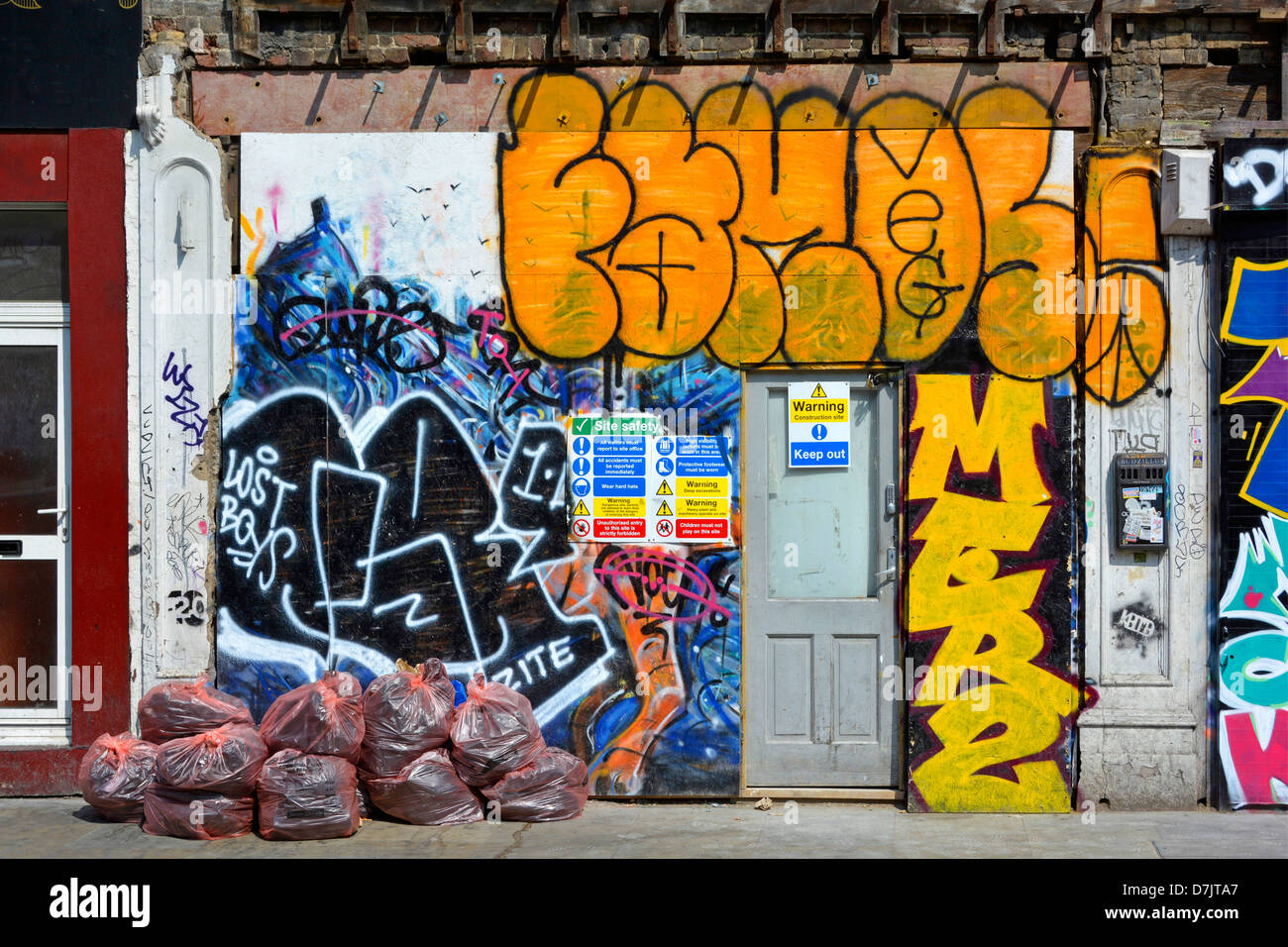 Ladenfront mit Brettern vernagelt und bedeckt in Graffiti Grafitti mit Müllsäcke und Bauunternehmen vor Ort Sicherheitshinweis Stockfoto