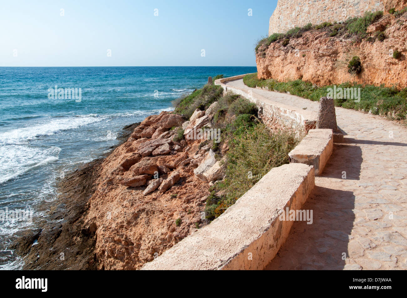 Gebogene Kopfsteinpflaster gesteinigt Weg schneiden durch weichen roten Felsen durch das Mittelmeer. Stockfoto