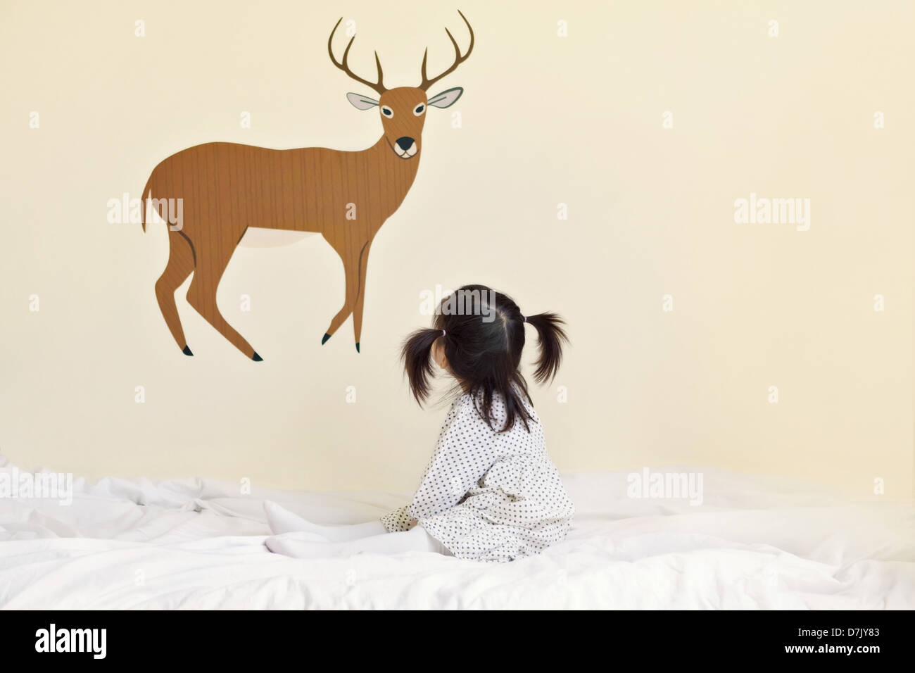 Niedliche koreanische amerikanische Mädchen mit Zöpfen auf Bett, Blick auf Abbildung der Hirsche mit dem Geweih Stockfoto