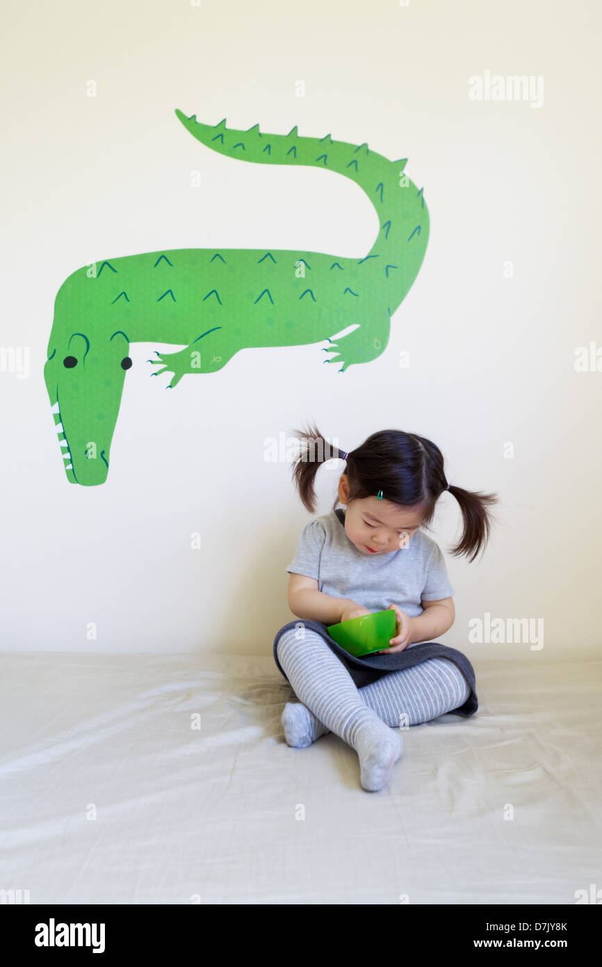 Korean American Girl Essen vom grünen Schale mit grünen Krokodil Wandkunst hinter Stockfoto