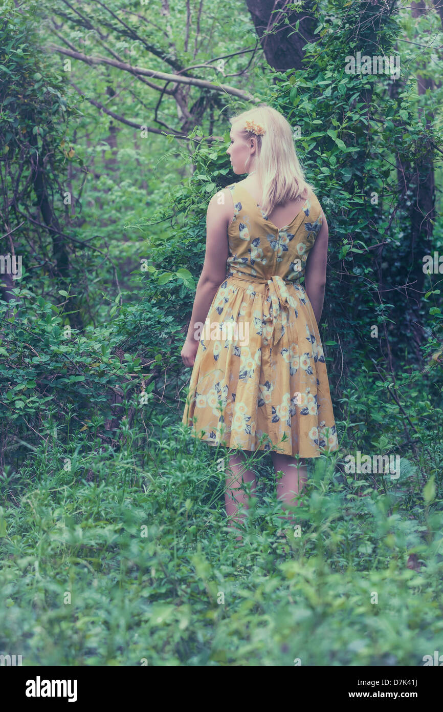 ein blondes Mädchen mit einem gelben Kleid im Wald Stockfoto