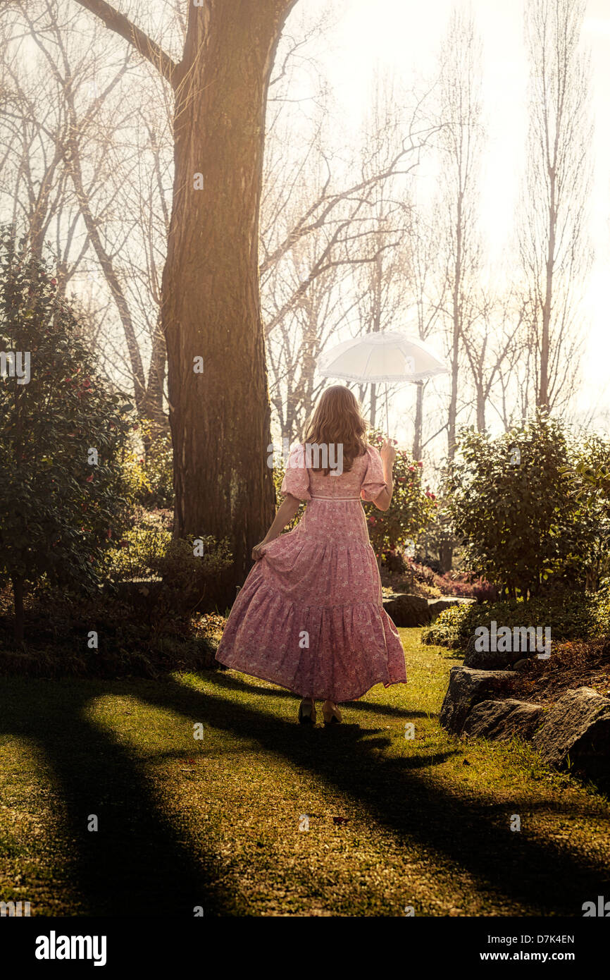eine Frau in einem geblümten Kleid mit einem Sonnenschirm ist in einem Park Fuß. Stockfoto