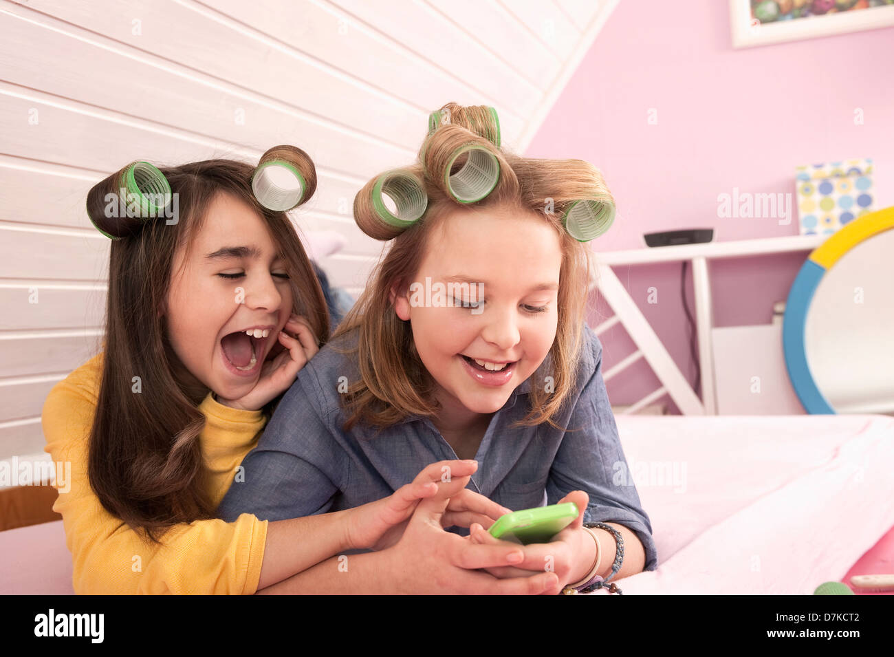 Mädchen mit Lockenwickler liegen und beobachtete Smartphone, Lächeln Stockfoto