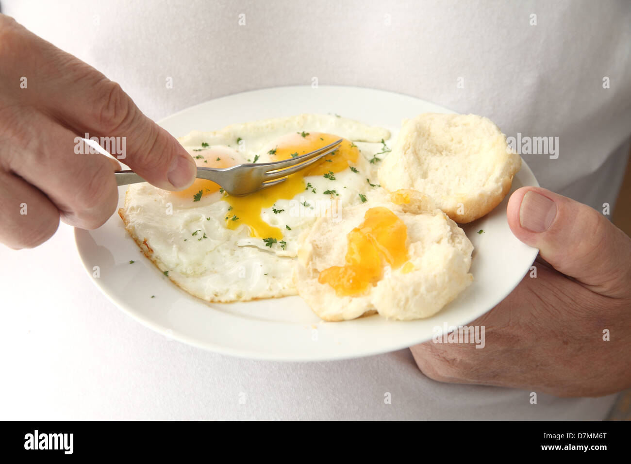 ein Mann isst seine Frühstückseier mit Keksen und Aprikosenmarmelade Stockfoto