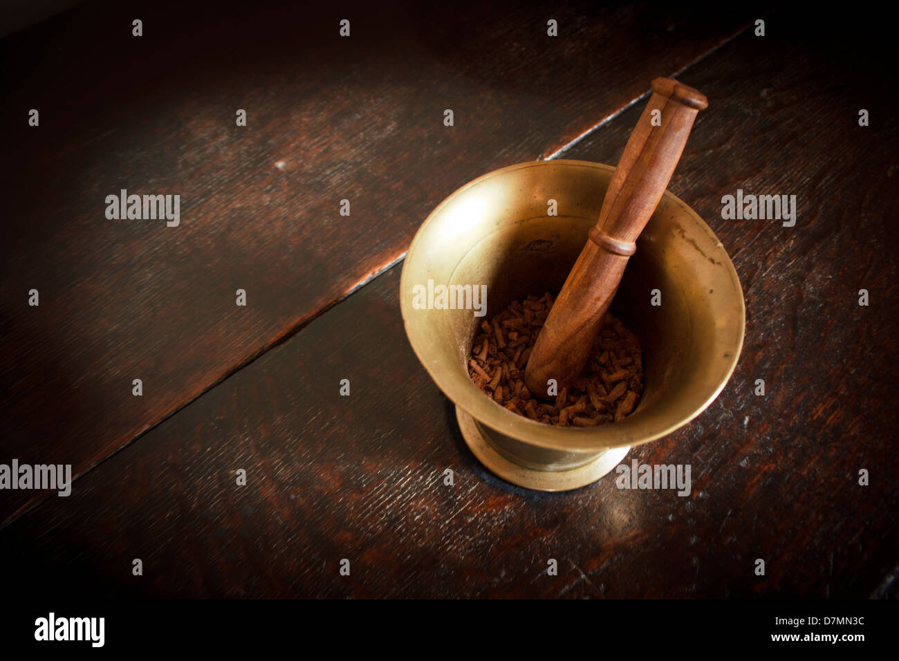 Eine alte Kupfer Mörser mit Hand geschnitzte hölzerne Stößel mit Nelken auf einen Eichentisch platziert. Stockfoto