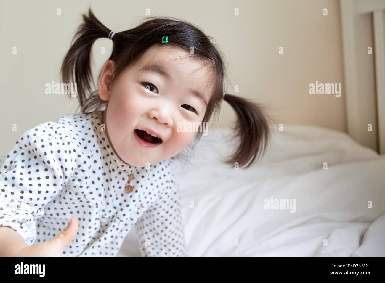 Korean American Kleinkind in Zöpfen lächelnd zu Kamera im Schlafzimmer Stockfoto