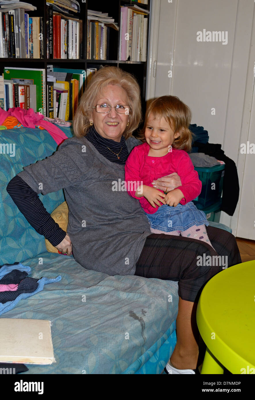 2 Jahre altes Mädchen sitzen auf blauem Sofa mit Großmutter und lächelnd Stockfoto