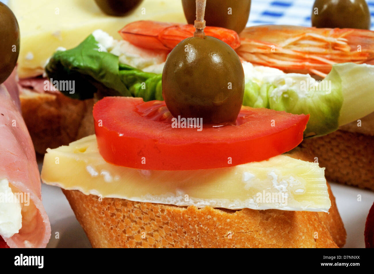 Spanische Tapas-Auswahl, mit Käse und Tomaten, garniert mit grünen Oliven und serviert auf knusprigem Brot im Vordergrund. Stockfoto