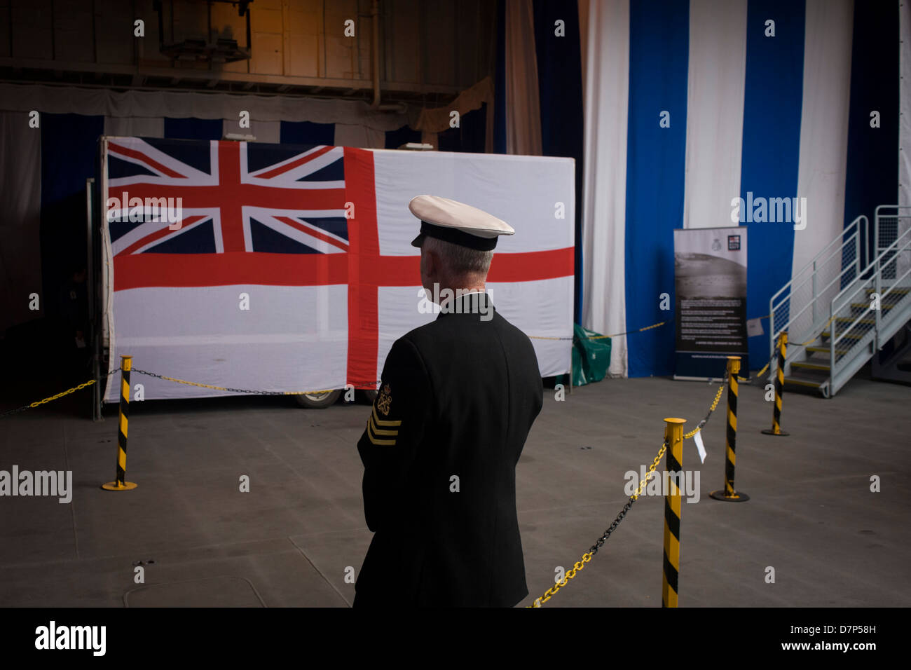 Ein Chief Petty Officer in der Nähe von der Navy Ensign Fahne Hangar deck während einer Tour durch die breite Öffentlichkeit an Bord Flugzeugträger der Royal Navy HMS Illustrious während eines öffentlichen Open-Tages in Greenwich. Illustrious angedockt an der Themse, so dass die Steuern zahlenden öffentlichen um den Decks vor seiner bevorstehenden Decommisioning zu erkunden. Navy Personal half mit dem PR-Event über die Mai Wochenende, historisch der Heimat England Flotte. Stockfoto