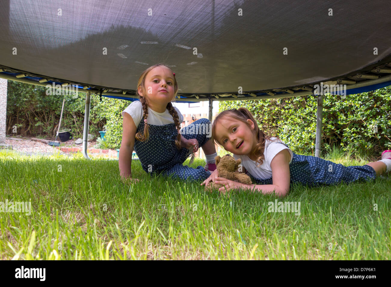 Schwestern, im Alter von 3 und 4, glücklich unter einem Trampolin im Garten spielen. Stockfoto