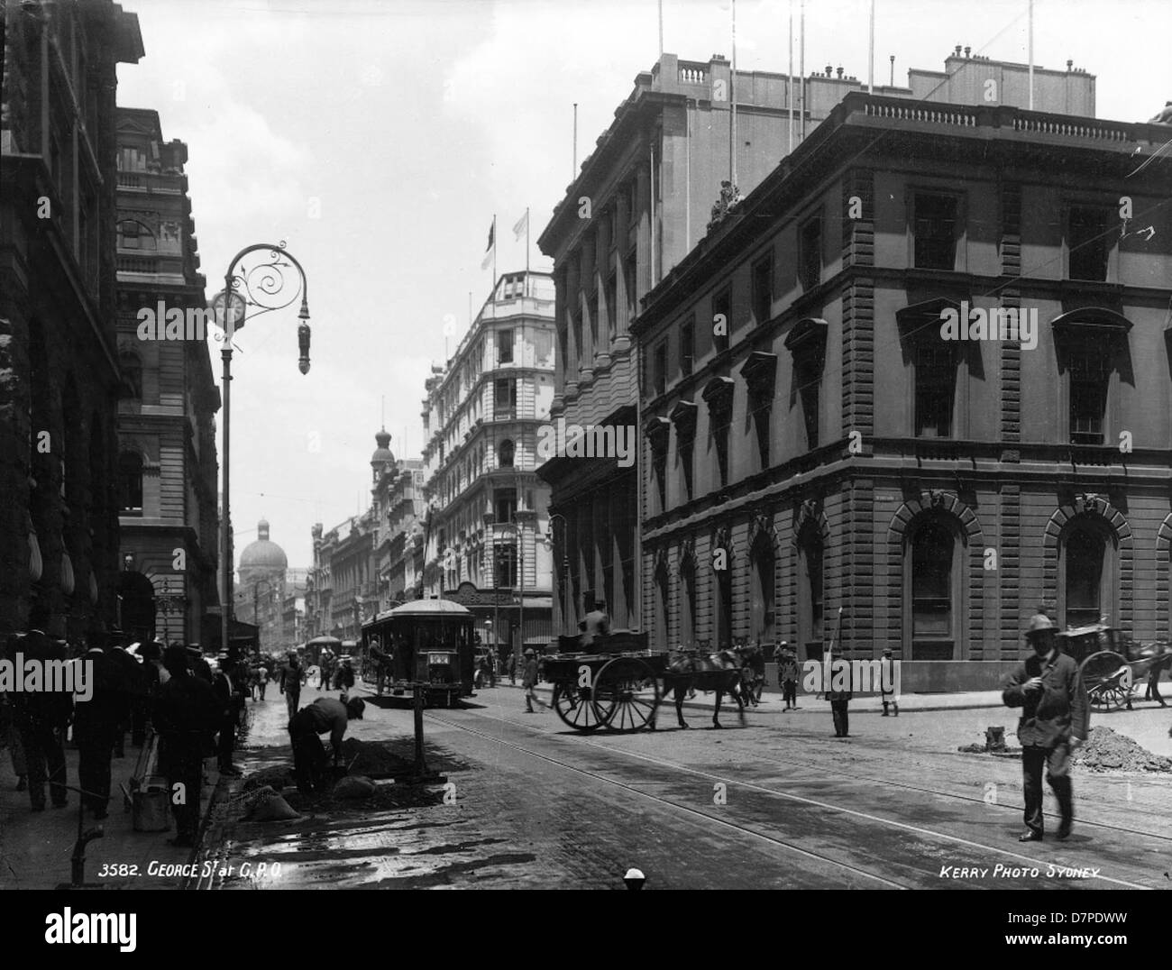 Dieses historische Schwarzweiß-Bild zeigt die George Street in Sydney mit dem General Post Office (GPO) und der Bank of New South Wales. Es zeigt die architektonische Entwicklung der Stadt und das geschäftige Straßenleben mit Kutschen, Arbeitern und Oldtimern aus einer früheren Zeit. Stockfoto
