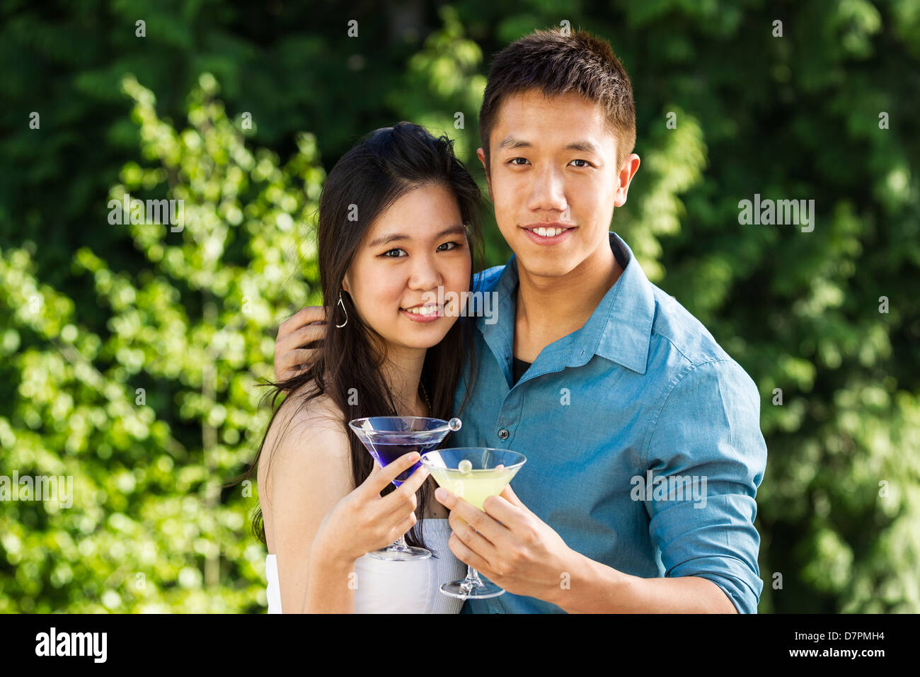Horizontale Foto eines jungen Erwachsenen Paares, Vorderansicht, hält Getränke im Freien mit grünen Bäumen im Hintergrund Stockfoto