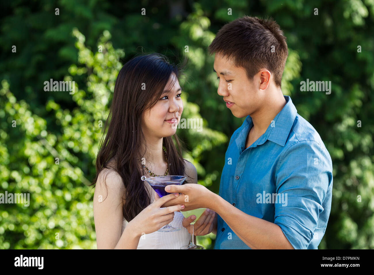 Horizontale Foto eines jungen Erwachsenen Mannes reichte seine Freundin einen Drink im Freien mit grünen Bäumen im Hintergrund Stockfoto