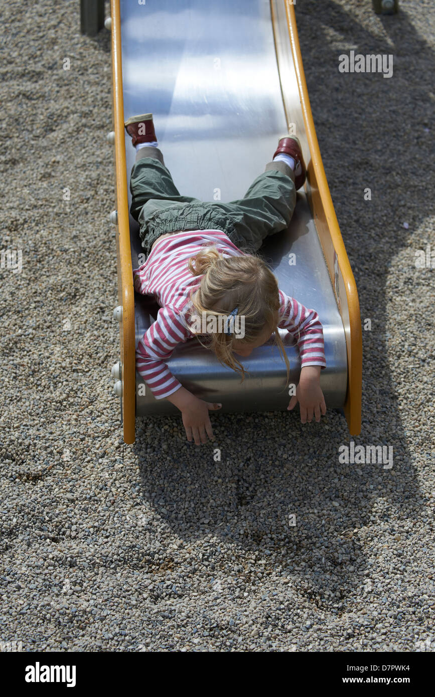 Blonde Mädchen Kind gleitende Folie auf einem Spielplatz Stockfoto