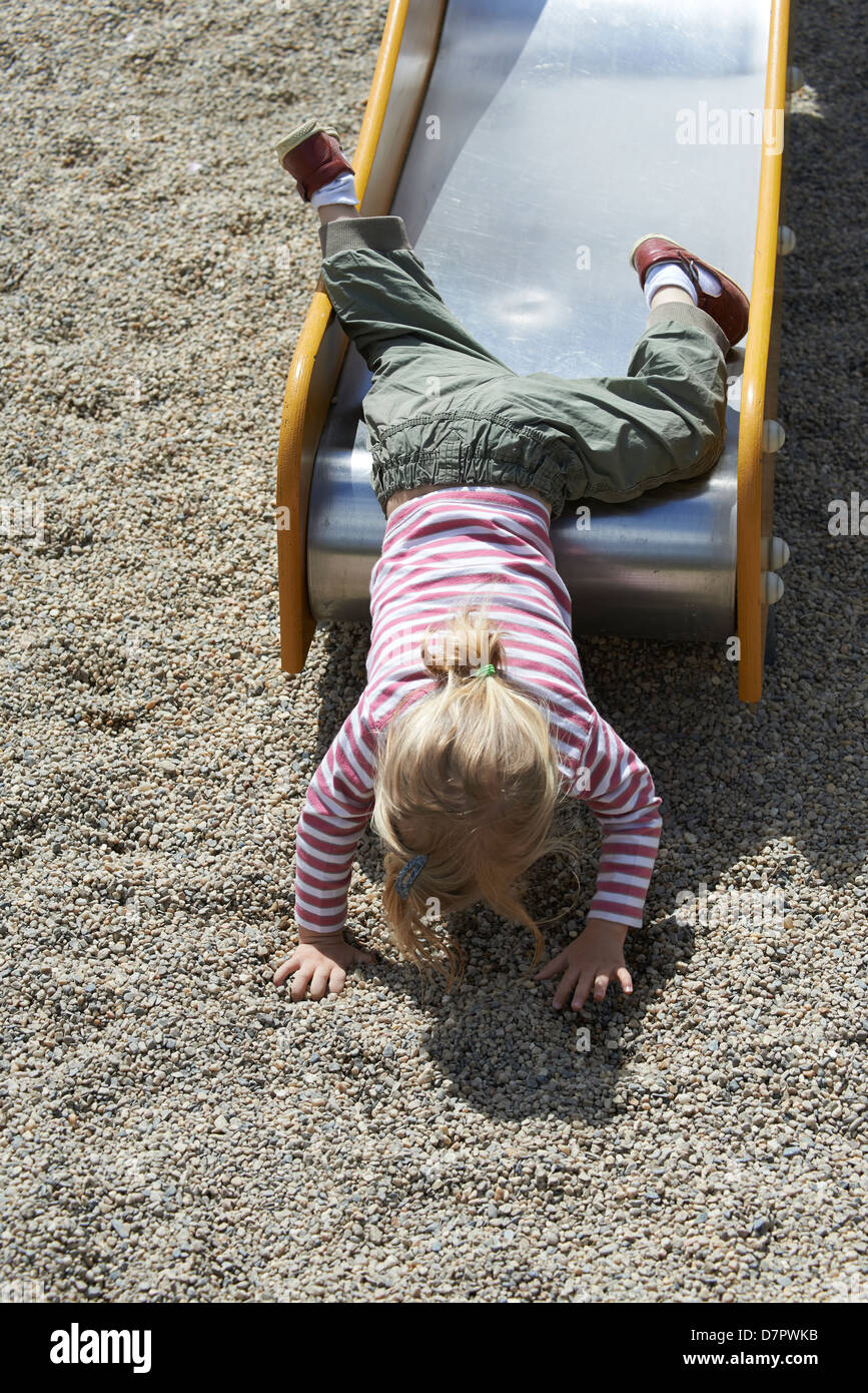 Blonde Mädchen Kind gleitende Folie auf einem Spielplatz Stockfoto