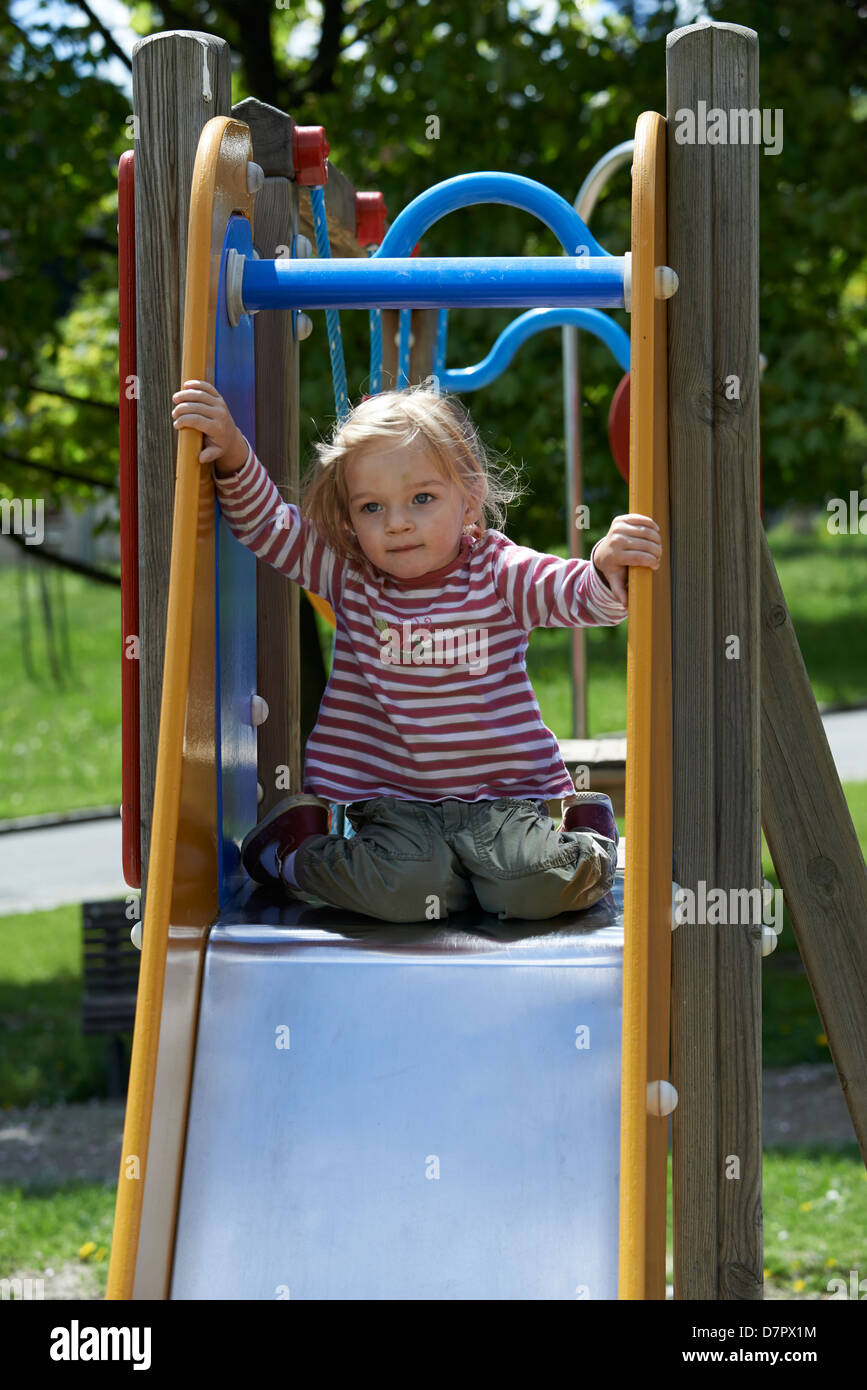 Blonde Mädchen Kind gleitende Folie auf einem Spielplatz Stockfoto